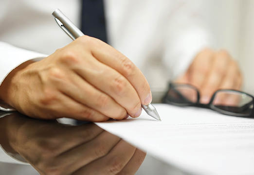 A close up shot of a man holding a pen and signing paperwork