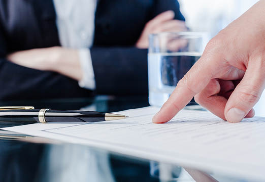 A business meeting with a close up photo of someone pointing to paperwork on a desk.